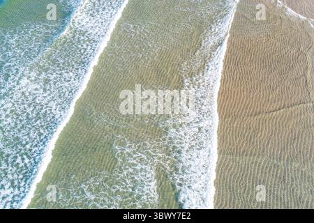 Luftaufnahme der Ozeanwellen, die über einem gewellten Sand Beach von oben nach unten über die Drohne springen Stockfoto