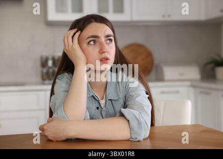 Verängstigte Frau, die an Paranoia leidet, am Tisch in der Küche Stockfoto