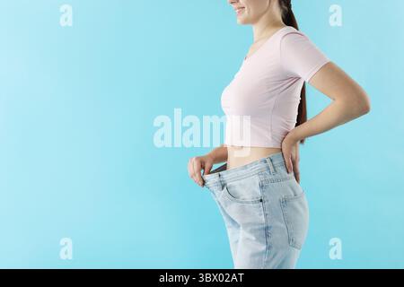 Frau trägt alte Jeans nach Gewichtsverlust auf hellblauem Hintergrund, Nahaufnahme. Leerzeichen für Text Stockfoto