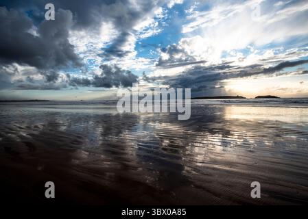 Sonnenuntergang an den riesigen Stränden von Essaouira mit blauem Himmel, weißen Wolken und Wellen, die am Ufer in Marokko zusammenbrechen Stockfoto