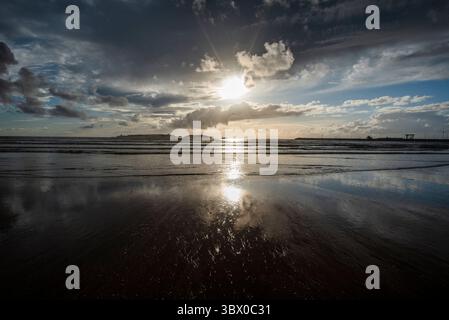 Sonnenuntergang an den riesigen Stränden von Essaouira mit blauem Himmel, weißen Wolken und Wellen, die am Ufer in Marokko zusammenbrechen Stockfoto