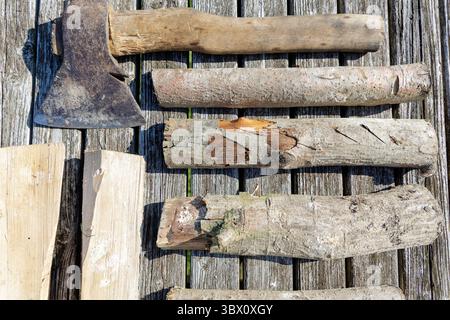 Ein Bild von einer alten Axt und mehreren Baumstämmen, die auf verwitterten Holzdielen angeordnet sind, heben Texturen und ein rustikales Thema hervor. Stockfoto