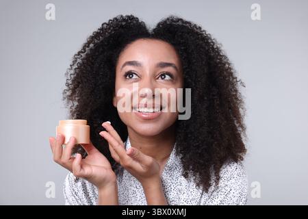 Schöne brasilianische Frau mit einem Glas Kollagencreme auf grauem Hintergrund Stockfoto