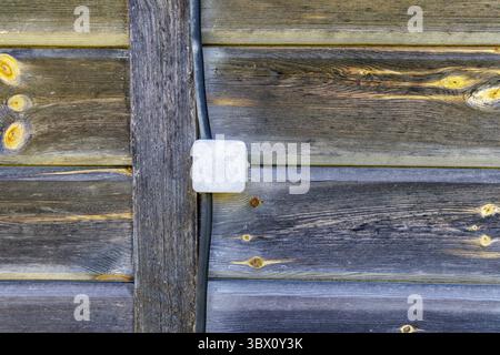 Eine strukturierte Nahaufnahme einer verwitterten Holzwand mit einem elektrischen Kabelkanal und einer Anschlussdose, die rustikale Details zeigt. Stockfoto