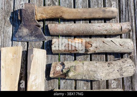 Ein Bild von einer alten Axt und mehreren Baumstämmen, die auf verwitterten Holzdielen angeordnet sind, heben Texturen und ein rustikales Thema hervor. Stockfoto