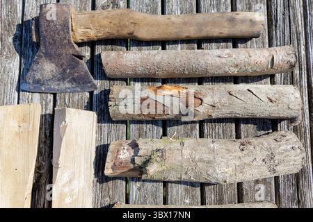 Ein Bild von einer alten Axt und mehreren Baumstämmen, die auf verwitterten Holzdielen angeordnet sind, heben Texturen und ein rustikales Thema hervor. Stockfoto