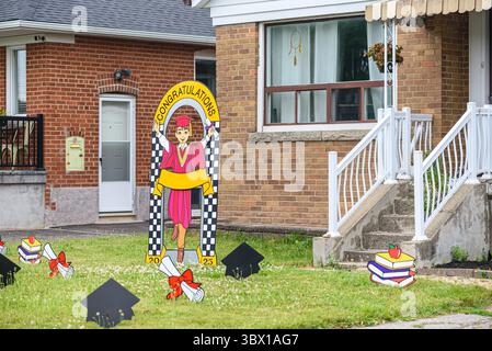 Der Rasen ist mit Pappausschnitten verziert, die eine Graduierung feiern, mit einer Comic-Graduierten-Figur unter einem Bogen „Congratulations 2025“, Büchern, Stockfoto