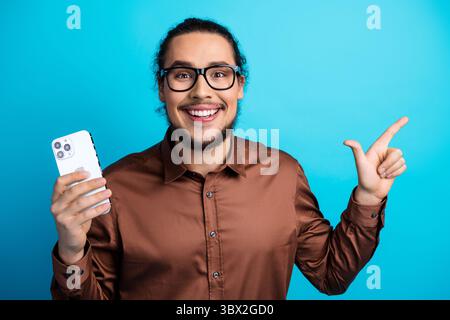 Glücklicher junger Profi, der ein Smartphone mit aufregender Begeisterung vor einem leuchtenden blaugrünen Hintergrund präsentiert Stockfoto