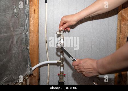Nahaufnahme der Hände einer Person mit einem Schraubenschlüssel zum Festziehen eines Verdichtungsventils an weißen PVC-Rohren in einer gerahmten Wand, die ein präzises Lot veranschaulicht Stockfoto