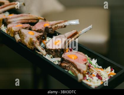 Saftige Lammkoteletts, serviert auf einem Bett aus buntem Gemüse mit lebhaftem Eigelb, das die visuelle Attraktivität des Gerichts unterstreicht. Stockfoto