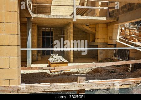 Teilweise erbaute Struktur mit Treppen, Raumteiler, Fenster- und Türöffnungen, Gerüsten, gelben Ziegelwänden, Schutt-Wagen und Holzbarrieren Stockfoto
