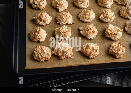 Frisch gebackene Makronen auf einem Pergament Line Sheet Pfanne: Geröstete Kokos- und Meringue-Kekse aus nächster Nähe auf mit Backpapier ausgelegtes Keksblatt Stockfoto