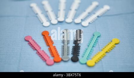 Nahaufnahme von mehrfarbigen kieferorthopädischen Bandbindern, die im Halbkreis auf einem strukturierten blauen Zahntuch angeordnet sind. Diese Gummibänder werden in oder verwendet Stockfoto
