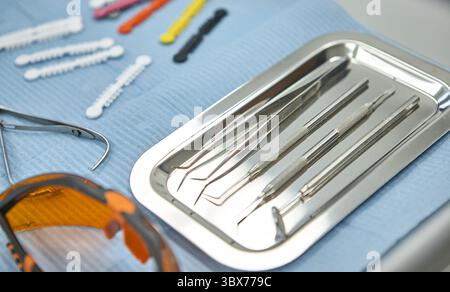 Nahaufnahme von Zahninstrumenten aus Edelstahl, die auf einem sterilen Tablett angeordnet sind, begleitet von orangefarbenen Schutzgläsern. Stockfoto