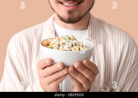 Mann, der eine Schüssel mit Müsliringen auf beigefarbenem Hintergrund hält, Großaufnahme Stockfoto