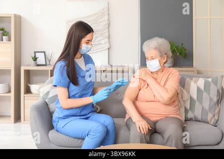 Junge Krankenschwester geimpft Seniorin auf Sofa zu Hause Stockfoto