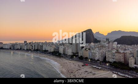 Luftaufnahme des Copacabana Beach in Rio de Janeiro bei Sonnenuntergang mit der Küste, den städtischen Gebäuden, dem Leme Hill und den fernen Silhouetten von Ipane Stockfoto