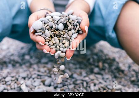 Frau, die Kieselsteine aus den Händen auf Rocky Beach gießt Symbol für Loslassen und natürliche Harmonie Stockfoto