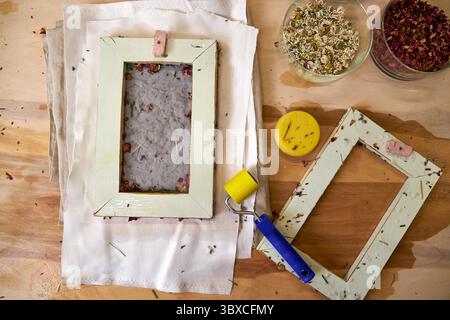Frisch gepresstes, handgemachtes Papier mit getrockneten Rosenblättern und Kräutern, zum Trocknen auf Stoff gelegt. DIY botanische Papierherstellung mit traditionellem Rahmen und natürlich Stockfoto