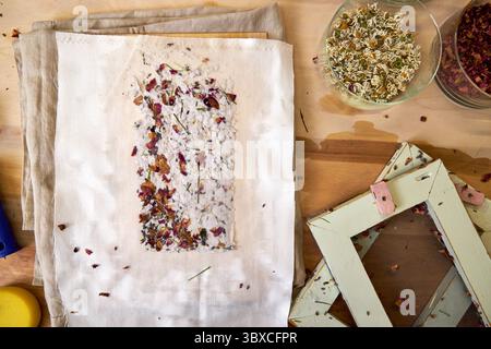 Frisch gepresstes, handgemachtes Papier mit getrockneten Rosenblättern und Kräutern, zum Trocknen auf Stoff gelegt. DIY botanische Papierherstellung mit traditionellem Rahmen und natürlich Stockfoto