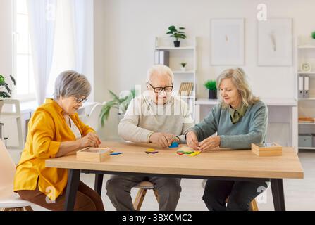 Ältere Menschen sitzen am Tisch, lösen Rätsel, beteiligen sich an kognitiver Aktivität im Pflegeheim. Stockfoto