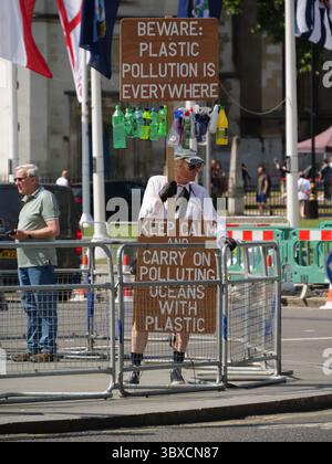 Ein Umweltaktivist steht vor den Houses of Parliament in Central London, Großbritannien, und hält ein Schild mit der Aufschrift „Vorsicht: Plastikverschmutzung ist überall“ und macht das Bewusstsein für die wachsende Gefahr von Kunststoffabfällen in städtischen und natürlichen Umgebungen. Stockfoto