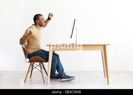 Aufgeregter schwarzer Mann, der Erfolg feiert, während er auf den Computer blickt Stockfoto
