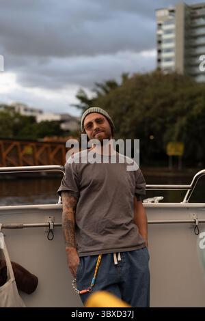 Mann mit Tattoos, der sich auf Fähren bei Sonnenuntergang in einer urbanen Umgebung entspannt Stockfoto