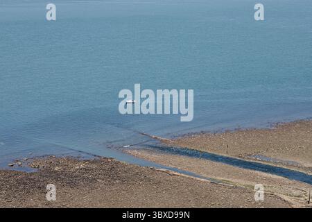 Ein Kiesstrand bei Ebbe. Die Flut ist völlig draußen und zeigt ein Steinfeld. Ein kleines Fischerboot auf dem Meer. Stockfoto