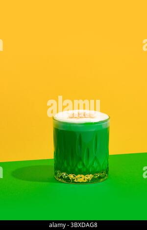 Pistazien-Latte mit schaumiger Oberseite aus Glas auf grünem und gelbem Hintergrund mit gemütlichem, hellem Styling Stockfoto