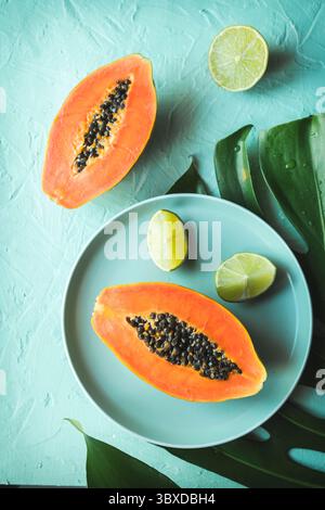 Ein flaches Lay-Bild, das eine reife, in zwei Hälften geschnittene Papaya und eine frische Limette auf einem großen tropischen Blatt zeigt Stockfoto