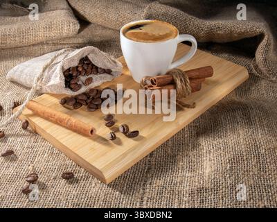 Dieses fesselnde Bild zeigt eine wunderschön gedämpfte Tasse Kaffee, verziert mit aufschäumender Milchkunst, elegant umgeben von frisch geröstetem Kaffee bea Stockfoto