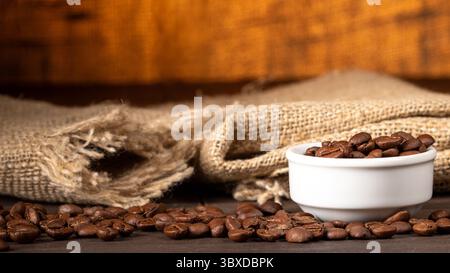 Dieses Bild zeigt eine mit Kaffeebohnen gefüllte Tasse auf einem Küchentisch, umgeben von verschütteten Kaffeebohnen. Warme Töne und rustikale cr-Einrichtung Stockfoto
