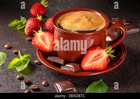 Eine gemütliche Szene mit einer warmen Tasse Kaffee auf einem rustikalen Holztisch, begleitet von frischen Erdbeeren und Stücken von reichhaltiger Schokolade, perfekt für einen DE Stockfoto