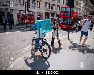 Ein Deliveroo Food-Kurier fährt mit einem Elektrofahrrad auf dem Bürgersteig in der City of London, Großbritannien, während die Diskussionen über städtische Zustelldienste, E-Bike-Vorschriften und Fußgängersicherheit in stark frequentierten Geschäftsbereichen zunahmen Stockfoto