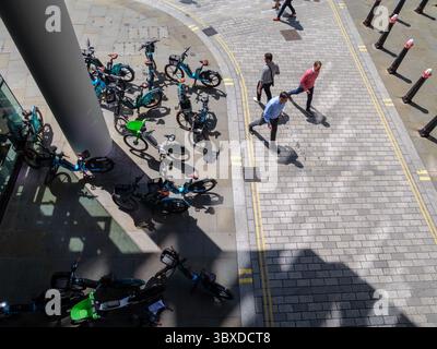 Fußgänger bewegen sich in der City of London, Großbritannien, um zahlreiche Mietfahrräder herum, die auf dem Bürgersteig herumlaufen, was die wachsende Besorgnis über die Behinderung des öffentlichen Raums durch Fahrräder ohne Dock hervorhebt. Stockfoto
