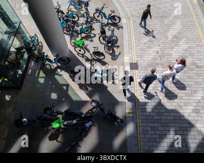 Fußgänger bewegen sich in der City of London, Großbritannien, um zahlreiche Mietfahrräder herum, die auf dem Bürgersteig herumlaufen, was die wachsende Besorgnis über die Behinderung des öffentlichen Raums durch Fahrräder ohne Dock hervorhebt. Stockfoto