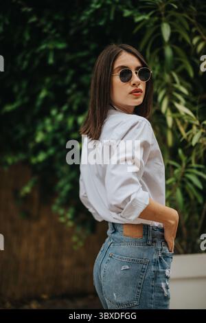 Modische junge Frau, die im Freien eine Sonnenbrille trägt, mit einer lässigen und selbstbewussten Atmosphäre Stockfoto