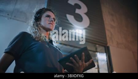 Weibliche Manager scannt Pakete mit Barcode-Scanner, mit Digital Tablet, arbeitet nachts. Verschiedene Mitarbeiter, die Kartonschachteln aus dem Logistiklager transportieren. Online-Bestellungen, Lieferung. Zeitlupe. Stockfoto