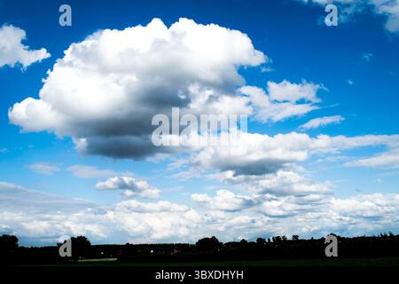Eine Weitwinkelaufnahme eines dynamischen blauen Himmels, gefüllt mit großen, flauschigen Kumuluswolken, die sich über einen dunklen ländlichen Horizont erstrecken und Gefühle der Weite wecken. Stockfoto
