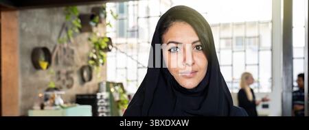 Selbstbewusste junge muslimische Frau in einem schwarzen Hijab, die in einem modernen Büro posiert. Porträt einer professionellen arabischen Geschäftsfrau mit Tradition A Stockfoto