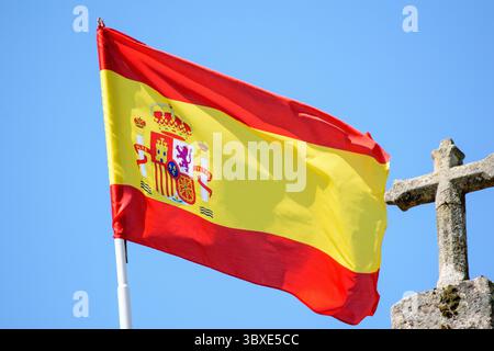 Spanische Flagge mit Wappen, die gegen einen klaren blauen Himmel fliegen. Stockfoto