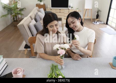 Seniorenmutter und erwachsene Tochter glücklich auf dem Tisch, während sie Blumen in einer Vase zusammen arrangieren. Technologie- und Lifestyle-Konzept. Glückliche gemeinsame Zeit Stockfoto