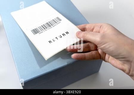 Die Hand einer Frau hält ein Rücksendeetikett über der blauen Box. Hochwertige Fotos Stockfoto