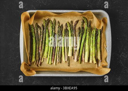 Geröstete Spargelstangen sind ordentlich auf einem mit Backpapier ausgelegten Blech angeordnet Stockfoto