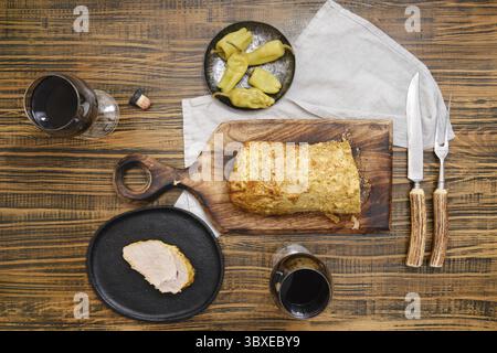 Blick von oben auf geröstetes Schweinefleisch und eingelegte Paprika auf einem Holztisch, begleitet von Rotwein in Gläsern Stockfoto