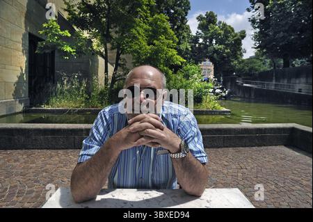 Porträt eines älteren Herrn mit Bart und Sonnenbrille, der an einem Tisch sitzt, im Hintergrund das Wasserspiel der Neuen Pinakothek, München, U Stockfoto