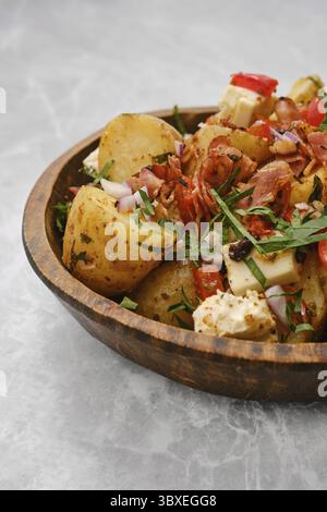 Eine Schüssel gefüllt mit gekochten Kartoffeln, gemischt mit frischem Gemüse, Kräutern, Speck und Käse. Das Gericht wird mit roten Zwiebeln und gehackter Petersilie garniert Stockfoto