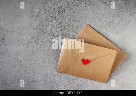 Basteln Sie Briefumschläge mit roten Papierherzen auf grauem Gips Stockfoto