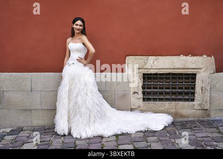 Wunderschöne Braut, die an einem Hochzeitstag ein wunderschönes elegantes weißes bodenlanges Kleid in einer alten schönen europäischen Stadt trägt Stockfoto